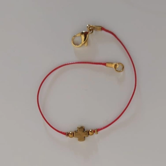 Bracelet sur cordon rouge avec croix en métal doré, porté au poignet